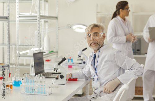 Senior scientist sitting at workplace in modern laboratory. Elderly professor posing for camera. Old grey-haired male researcher carrying out scientific research. Microbiology and biotechnology