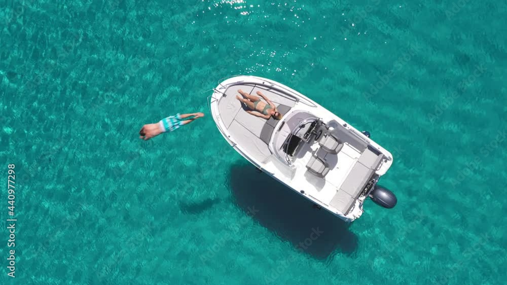 Aerial - Young couple relaxing on a boat on a beautiful turquoise sea Aerial - Young couple relaxing on a boat on a beautiful turquoise sea