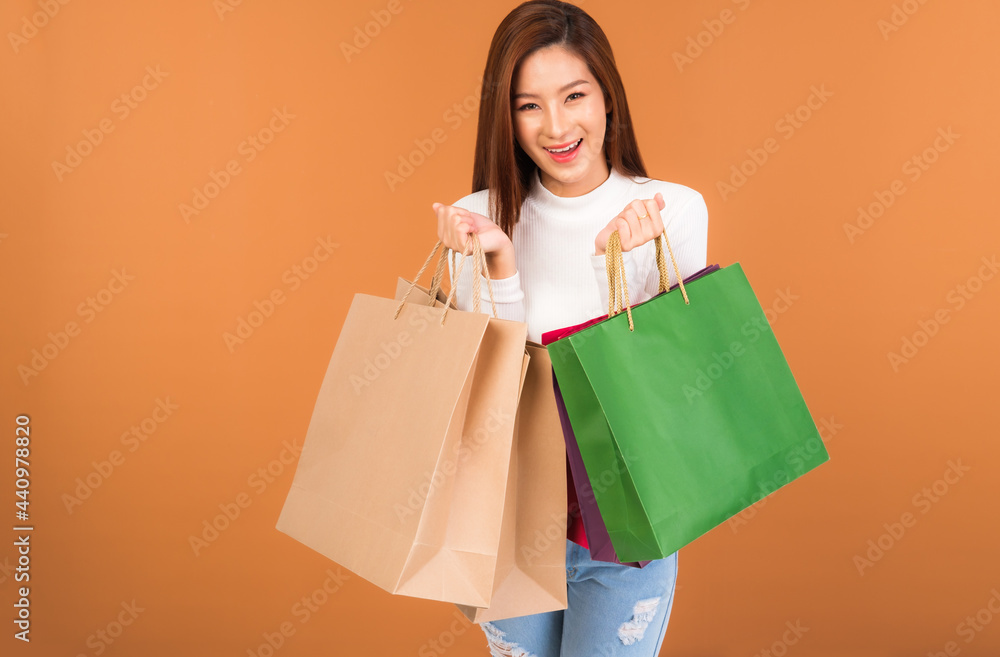 Beautiful young Asian woman wearing a white silk blouse, jeans, holding a shopping bag, smiling with a good mood, cheerful and cheerful in Holiday at the mall Center. With a brown background. Beautiful young Asian woman wearing a white silk blouse, jeans, holding a shopping bag, smiling with a good mood, cheerful and cheerful in Holiday at the mall Center. With a brown background.