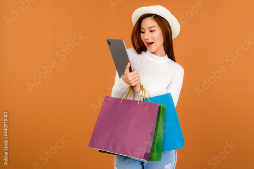 A beautiful Asian woman wearing a white long sleeve sweater and jeans, carrying a paper bag with items bought and tablet from a department store.