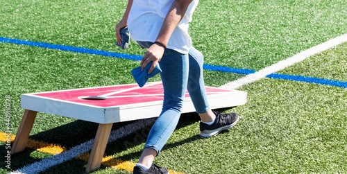 Fotografiet Person throwing a bean bag while playing cornhole on a turf field
