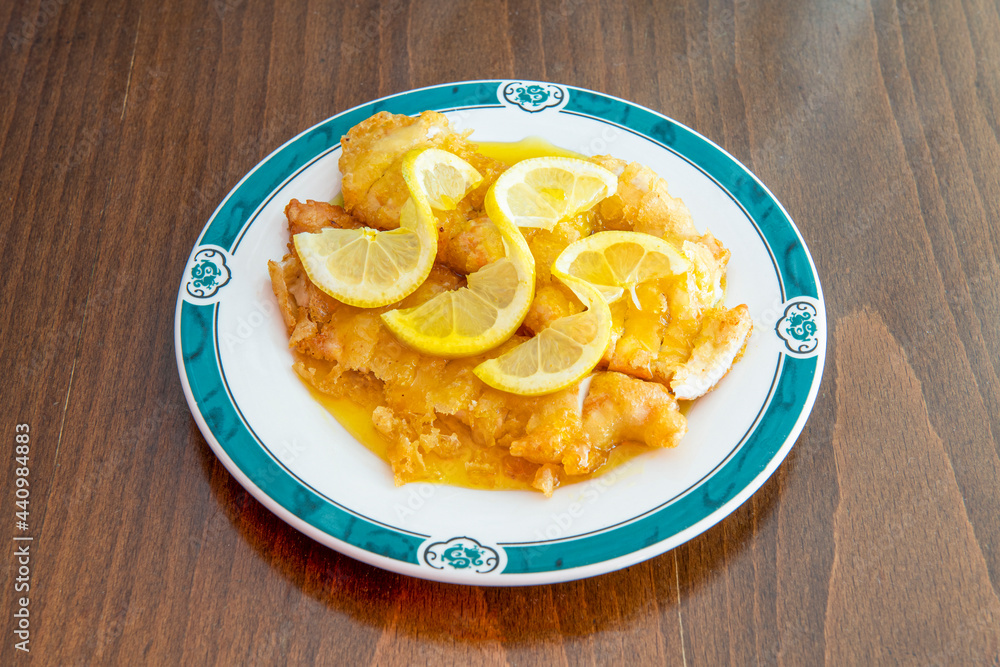 Breaded chicken fillets soaked in Chinese lemon sauce on white plate and brown wooden table Breaded chicken fillets soaked in Chinese lemon sauce on white plate and brown wooden table