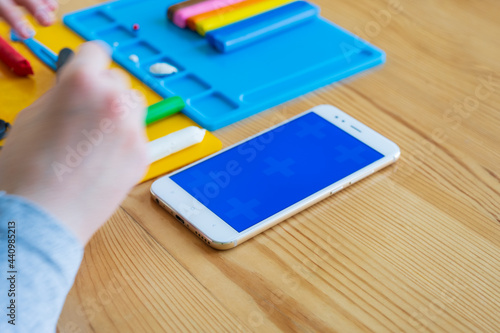 Children's hands during modeling from plasticine, mobile phone with chroma key blue screen. Space for text