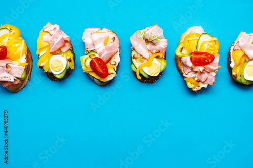 Trendy open sandwiches with cream cheese, quail eggs, tomatoes, bacon and vegetables. Modern, summer still life of healthy snacks. Flat lay in minimalism style. Smorrebrod with various stuffing.