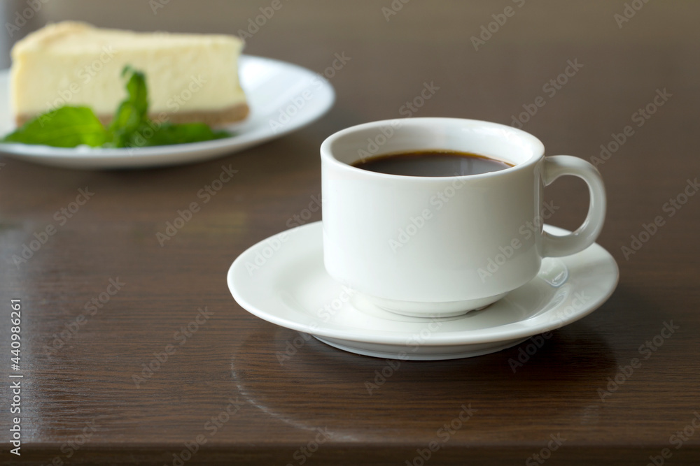 Cup with freshly brewed coffee and a slice of cheesecake on the table in a cafe Cup with freshly brewed coffee and a slice of cheesecake on the table in a cafe