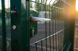 Handle with a lock on the open gate of a sports ground fenced with a welded mesh fence, outdoors, at sunset. Close-up.