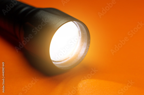 Black Flashlight and a ray of light on the orange background. Close up photo.