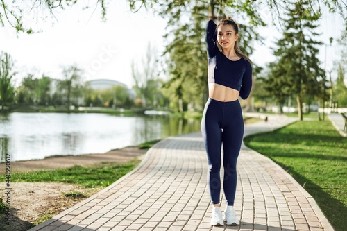Fit young girl in dark blue sportswear exercising in park