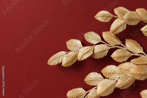 The branch with leaves is made of straw. Straw wall decoration. The products are made of straw. Decoration of straw on a red background