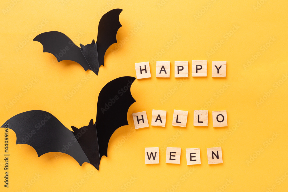 Halloween flat lay with text Happy Halloween and two flying bat on yellow background