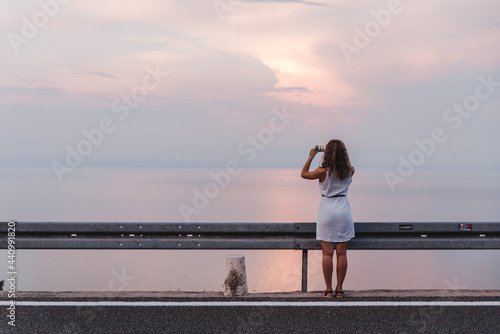 stop on the road woman taking picture on the phone of sunset above the sea