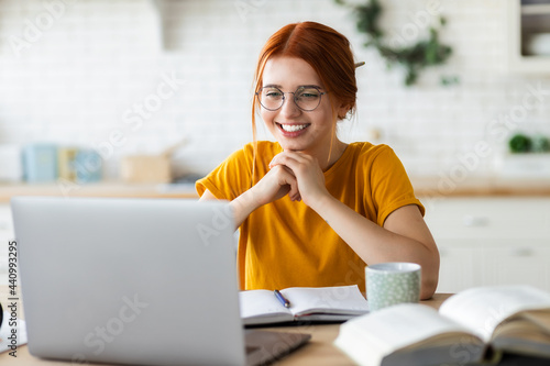 Online learning, portrait of red-haired happy caucasian female freelancer or smiling woman student using a laptop for a video call with a teacher, distance education concept photo