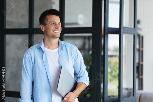 Headshot portrait of  caucasian successful freelancer or student with laptop in casual clothes, stands in office or college, smiling, business concept