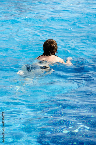 Caucasian brunette woman swims in pool with copy space. Female enjoys relaxing in blue water. Summer vacation concept. Person chills in cool water of swimming pool.