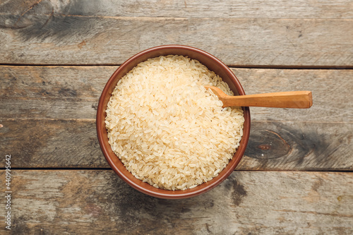Bowl with raw rice on wooden background