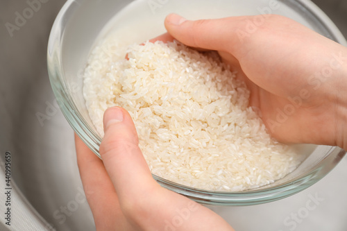 Slika na platnu Woman rinsing rice in glass bowl under running water, closeup