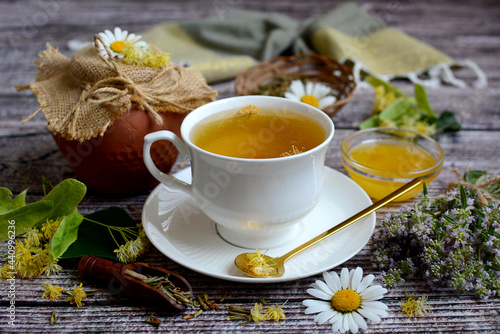 Composition of medicinal herbs. white cup with herbal tea, linden flowers, thyme, honey and chamomile flowers on a wooden background