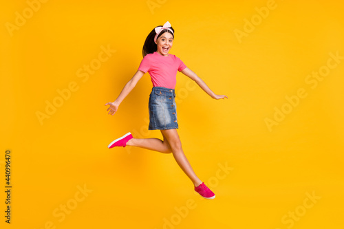 Photo of impressed shiny school girl wear pink t-shirt smiling jumping high isolated yellow color background