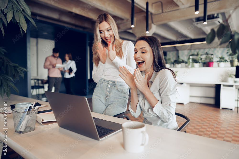 Two young happy businesswomen celebrating project success in office Two young happy businesswomen celebrating project success in office
