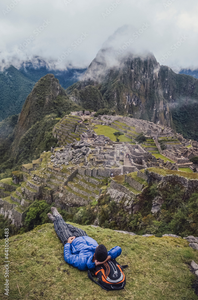 Young man laying down, contemplating Machu Picchu lost city with Huayna Picchu mountain. Ruins of ancient inca civilization in the sacred valley of Cusco Province. Peru, South America