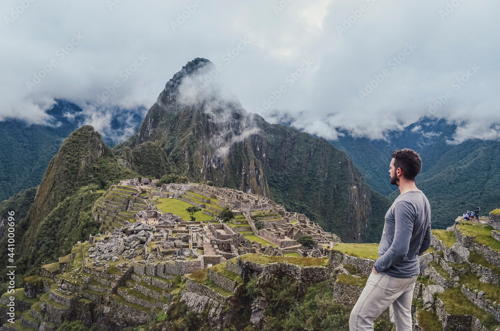 Young man standing, contemplating Machu Picchu lost city with Huayna Picchu mountain. Ruins of ancient inca civilization in the sacred valley of Cusco Province. Peru, South America Young man standing, contemplating Machu Picchu lost city with Huayna Picchu mountain. Ruins of ancient inca civilization in the sacred valley of Cusco Province. Peru, South America