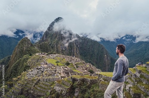 Young man standing, contemplating Machu Picchu lost city with Huayna Picchu mountain. Ruins of ancient inca civilization in the sacred valley of Cusco Province. Peru, South America