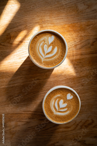 Coffee on wooden background. Two cups of cappuccino with latte art on brown table with sunbeam. Fresh morning coffee with delicious milk foam. Top view, flat lay.