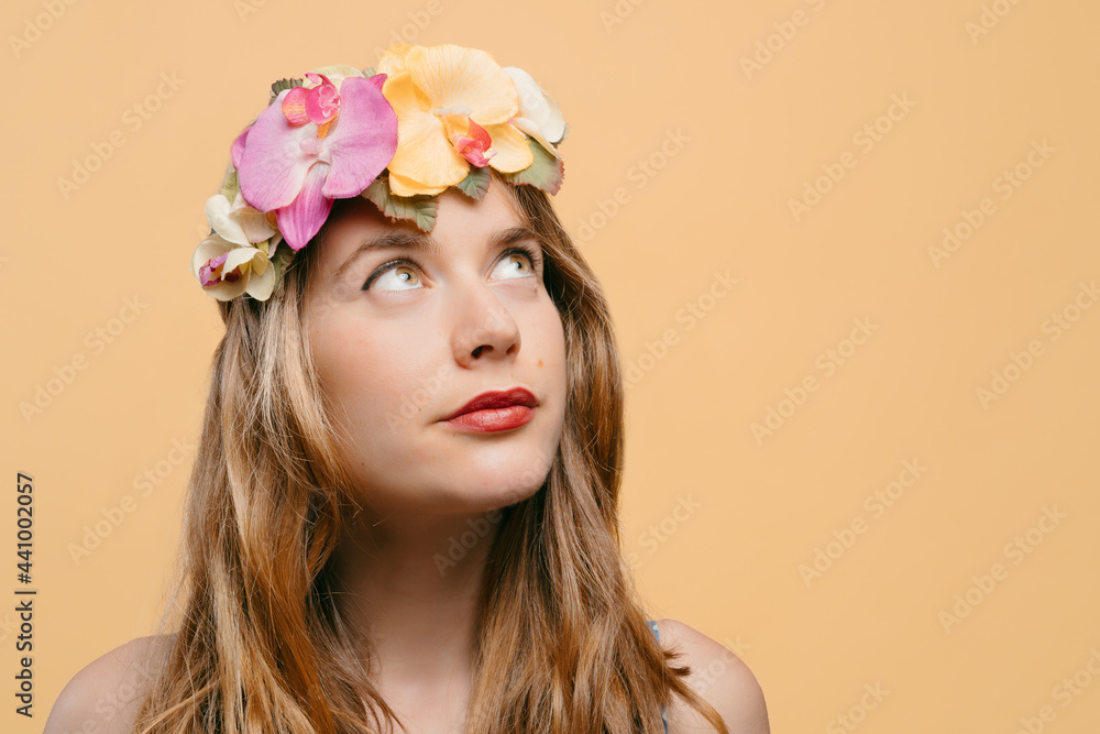Portrait of a young blonde girl with a headband of flowers and plants on her head looking upwards on a yellow background. summer and nature concept. copy space Portrait of a young blonde girl with a headband of flowers and plants on her head looking upwards on a yellow background. summer and nature concept. copy space