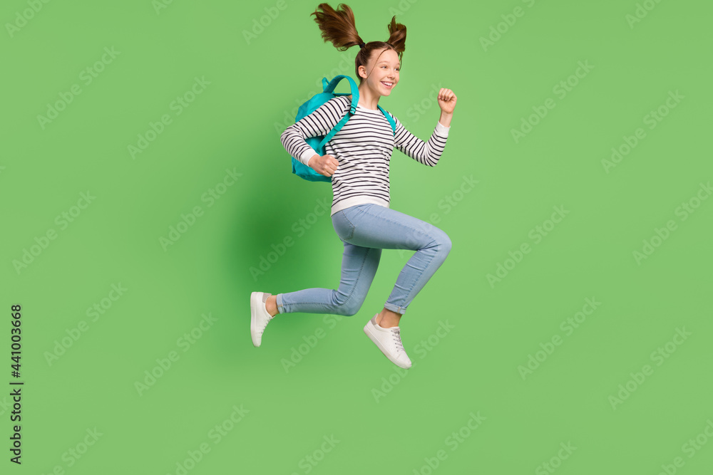 Photo of hurrying cute small schoolgirl dressed striped sweater rucksack running jumping empty space isolated green color background Photo of hurrying cute small schoolgirl dressed striped sweater rucksack running jumping empty space isolated green color background
