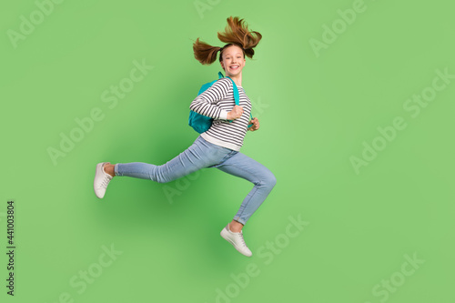Fototapeta Naklejka Na Ścianę i Meble -  Photo of cute charming small schoolgirl dressed striped sweater rucksack running jumping high isolated green color background