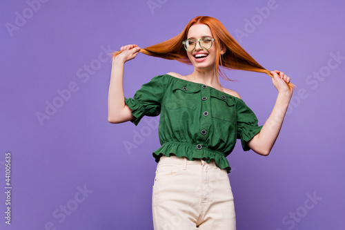 Photo of cool red millennial lady hold hair wear eyewear green bare shoulders blouse isolated on violet background