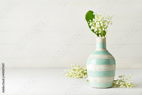 Vase with beautiful lily-of-the-valley flowers on light wooden background