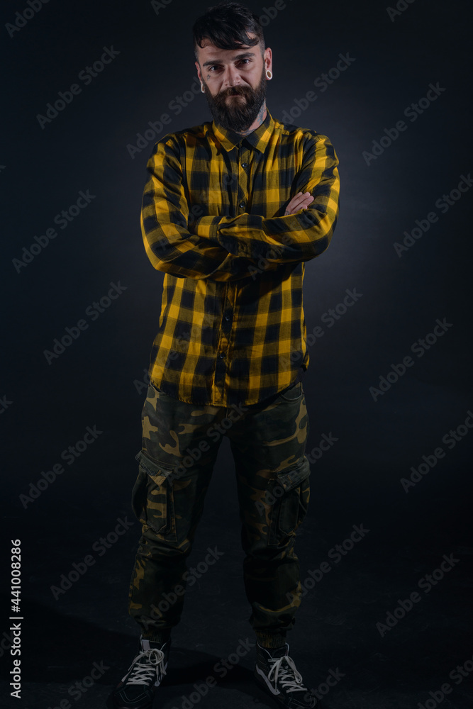 Full-length portrait of an attractive man with tattoos posing dressed in yellow and black checkered shirt on a black background Full-length portrait of an attractive man with tattoos posing dressed in yellow and black checkered shirt on a black background