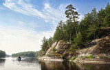 man rows on boat in beautiful nordic rocky bay. Big slanted pine on granite cliff. Baltic sea, gulf of Finland