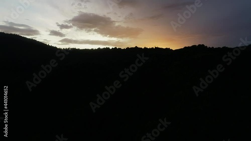 Aerial view of sunset over the Mountain range silhouette. Drone cinematic shot of mountains at orange sunset in summer. Sun rays. Dark sunrise aerial view of Carpathian Mountain in Ukraine.