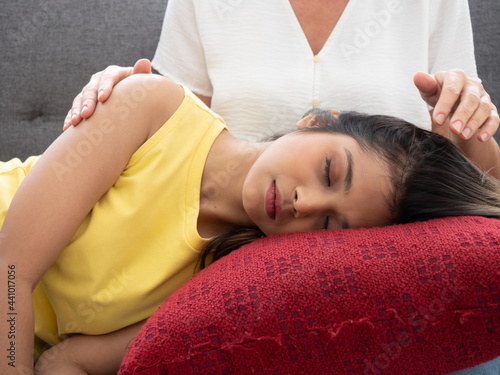 Fotografie The adopted caucasian mother care of her Asian teen daughter while she is sleeping on his lap