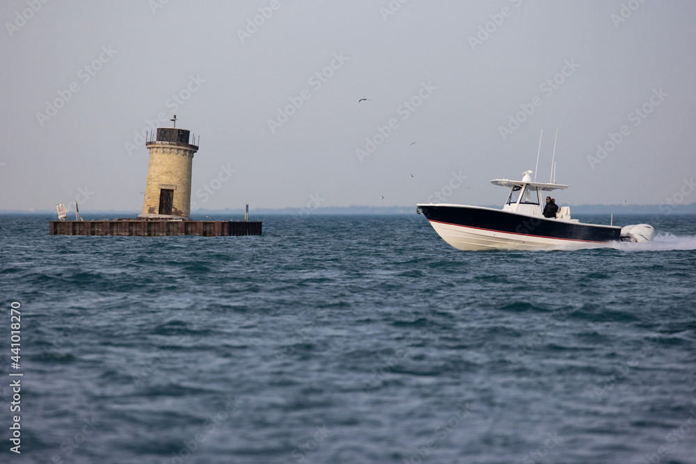 boat crossing a lake in front of a lighthouse.