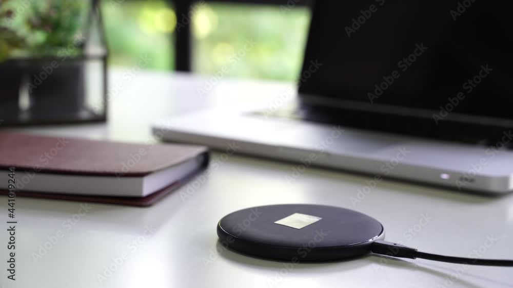 Smart phone being charged on wireless charger alongside with laptop, glasses, and notebook on table - Modern technology lifestyle concept