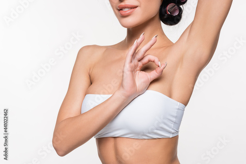 partial view of young woman showing smooth armpit with okay gesturing with hand isolated on white. photo