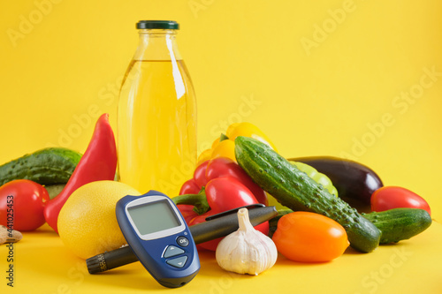 Digital glucometer and vegetables on yellow background. Diabetes diet