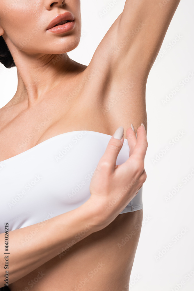 partial view of young woman in white top touching smooth armpit with hand isolated on white.