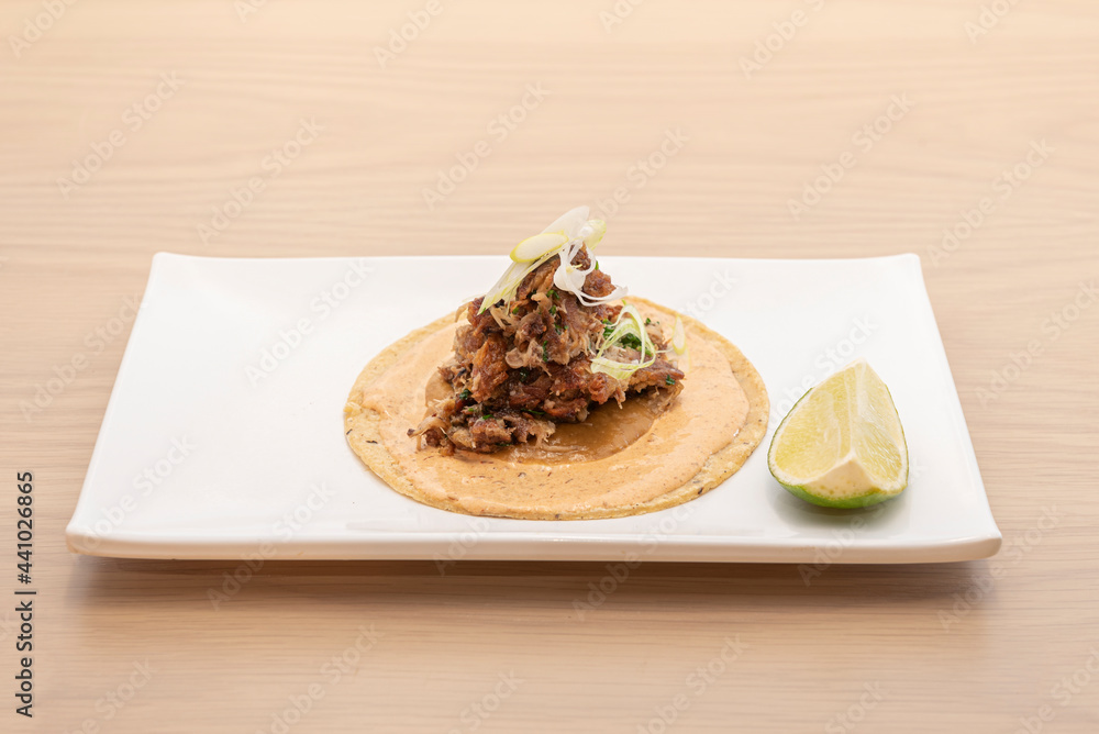 Lamb meat taco with vegetables and sauce and a wedge of lime on a white plate