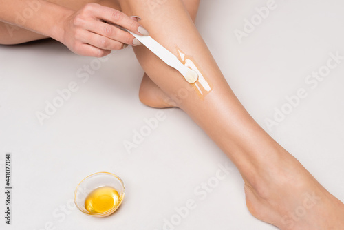 close up view of young woman making epilation on leg near bowl with honey on white.