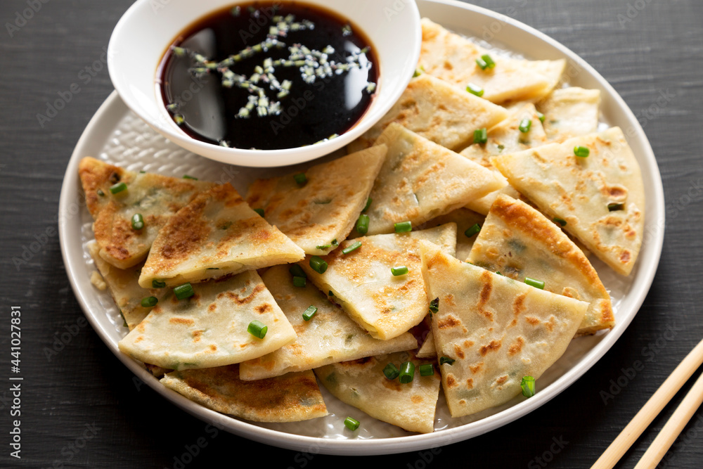 Homemade Scallion Pancakes with Soy Dipping Sauce on a black surface, side view.