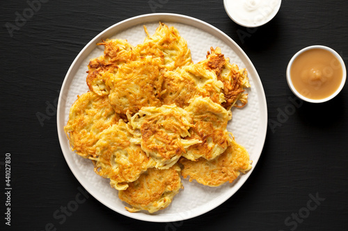Homemade Potato Pancakes Latkes with Apple Sauce and Sour Cream on a black background, top view. Flat lay, overhead, from above.