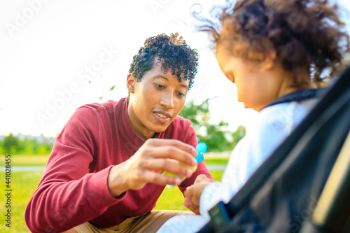 african american father and little girl are useing an ntibacterial gel in summer park outdoors photo