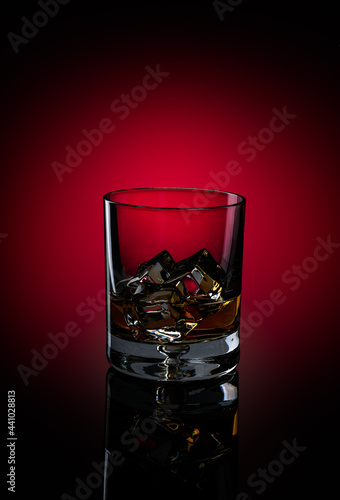 Glass of Kentucky Bourbon with ice on reflective surface on black background with circular red spot