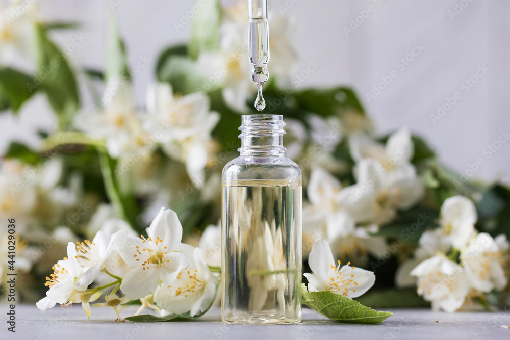 Jasmine essential oil in a glass dropper on a background of jasmine flowers. Jasmine essential oil in a glass dropper on a background of jasmine flowers.