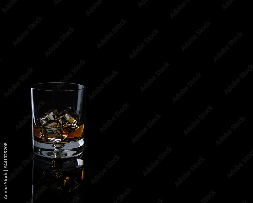 Glass of Kentucky Bourbon on rocks on black background with reflection on dark surface and space for copy text on the right side Glass of Kentucky Bourbon on rocks on black background with reflection on dark surface and space for copy text on the right side