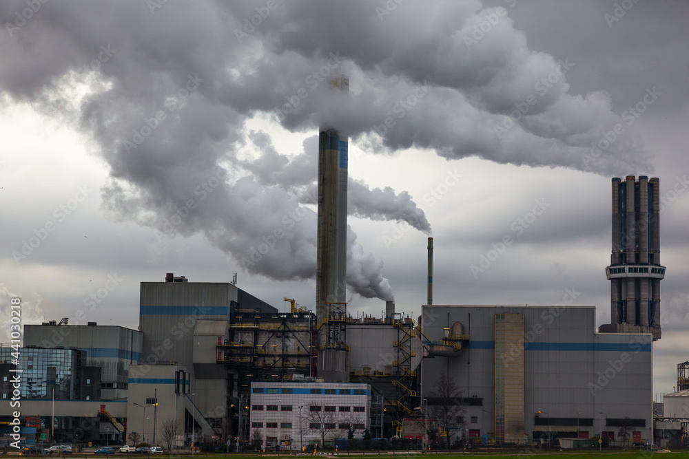 An industrial plant with chimneys from which thick smoke comes out into a cloudy sky. Environmental pollution by industry.